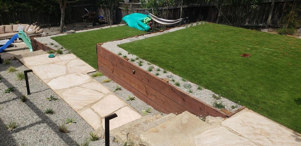 Backyard landscape featuring a green lawn, stone pathways, and a hammock setup.