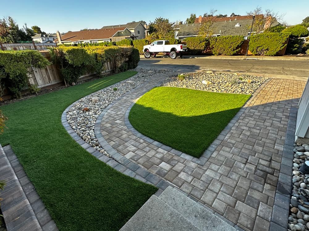Landscaped yard with artificial grass, gravel path, and colorful shrubs in a residential area.