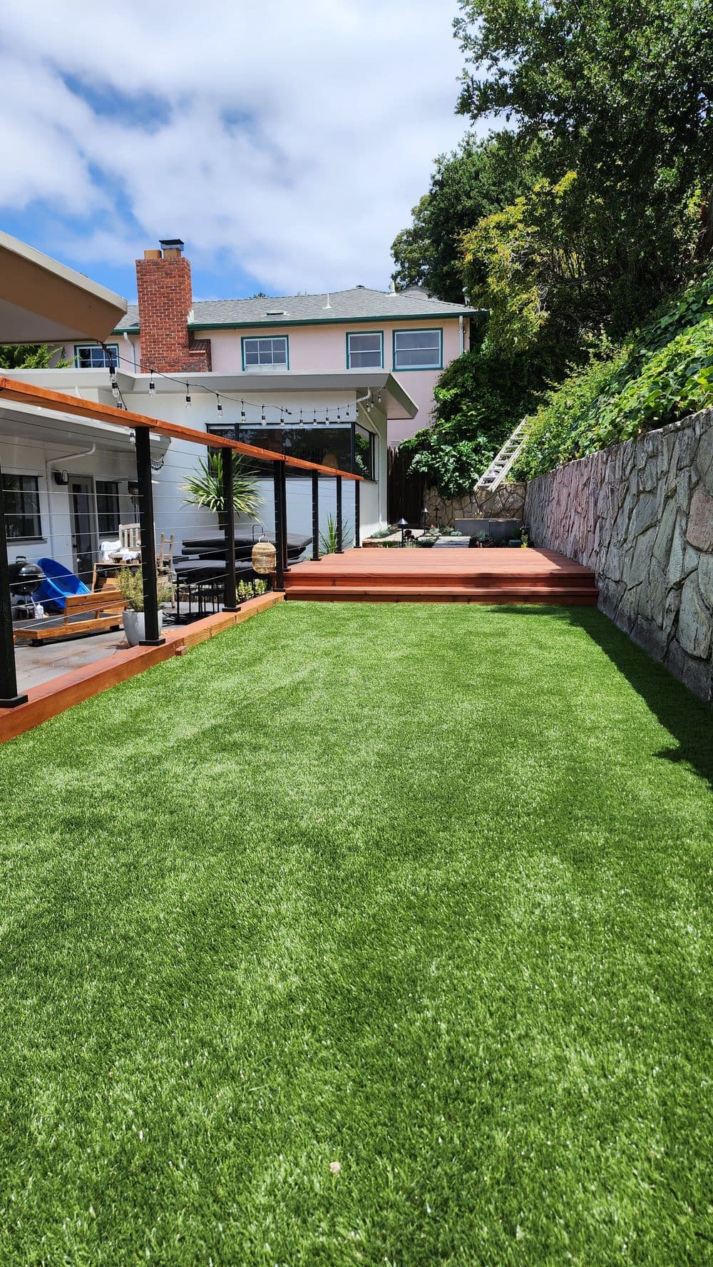 Lush green artificial grass yard with a stone wall and deck in a residential setting.