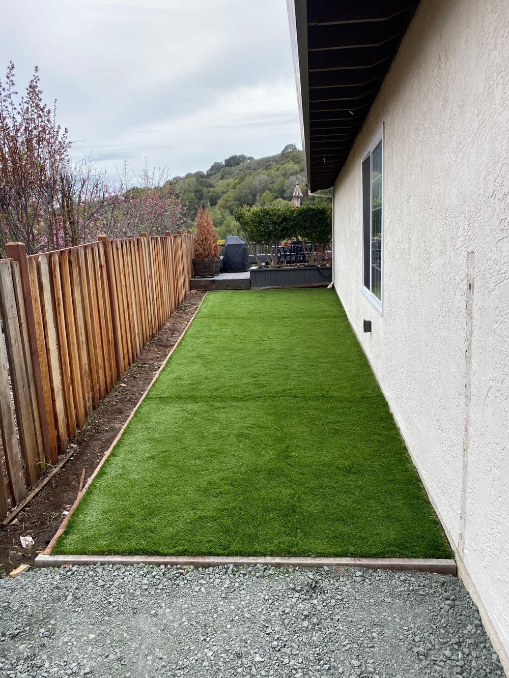 Lush green artificial turf installation next to a house and wooden fence.