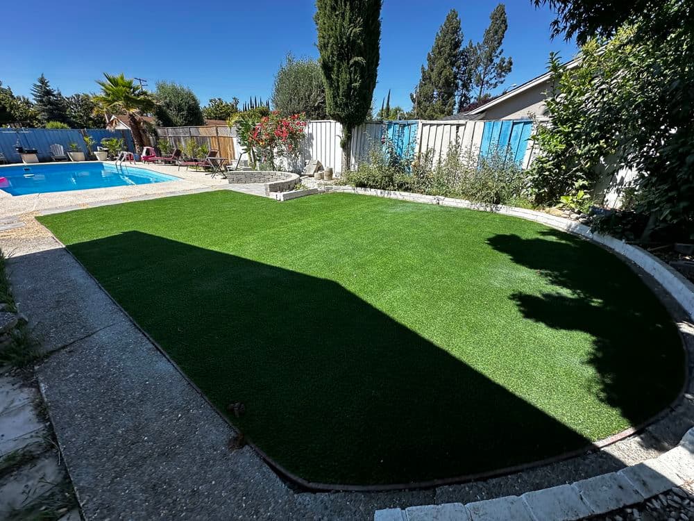Lush green artificial lawn with poolside and landscaped garden in sunny backyard.