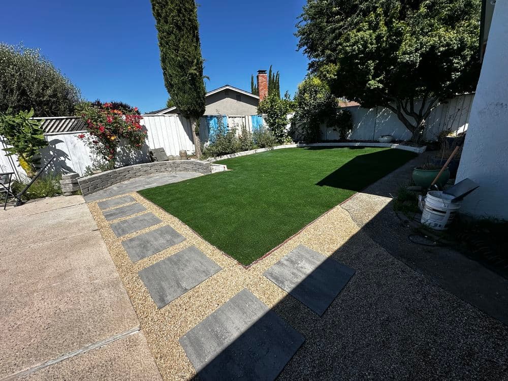 Lush green artificial turf in a landscaped backyard with stone pathways and sunny blue sky.