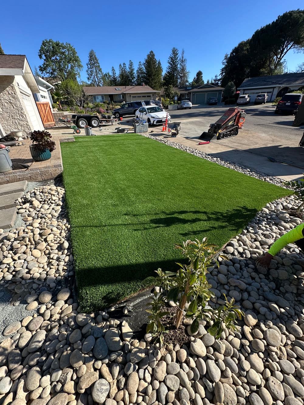 Lush green artificial turf installation with landscaped stones and plants in sunny residential yard.