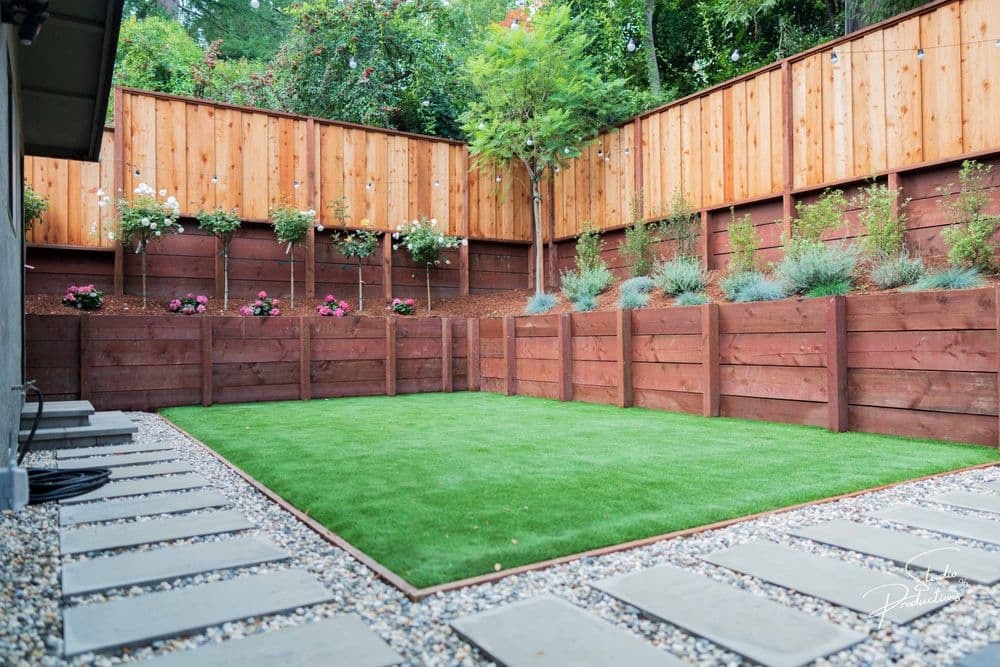 Modern backyard with artificial grass, wooden fence, and flower garden beds. Perfect for landscaping ideas.