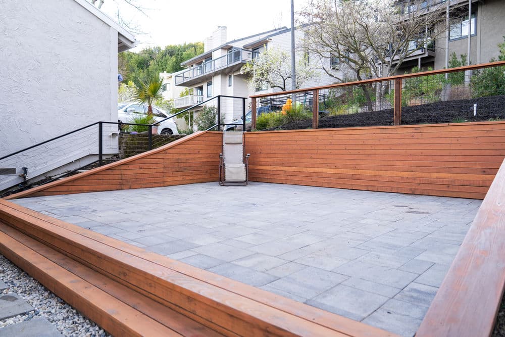 Wooden terrace with stone pavers in a residential backyard surrounded by greenery.