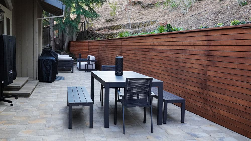 Modern outdoor patio with dining table, benches, and wooden privacy fence.