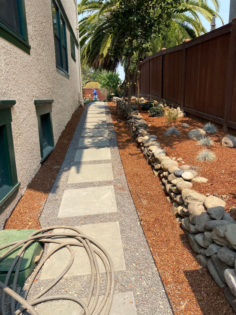 sidewalk pathway with stone steps, landscaped garden, and palm trees along a residential fence