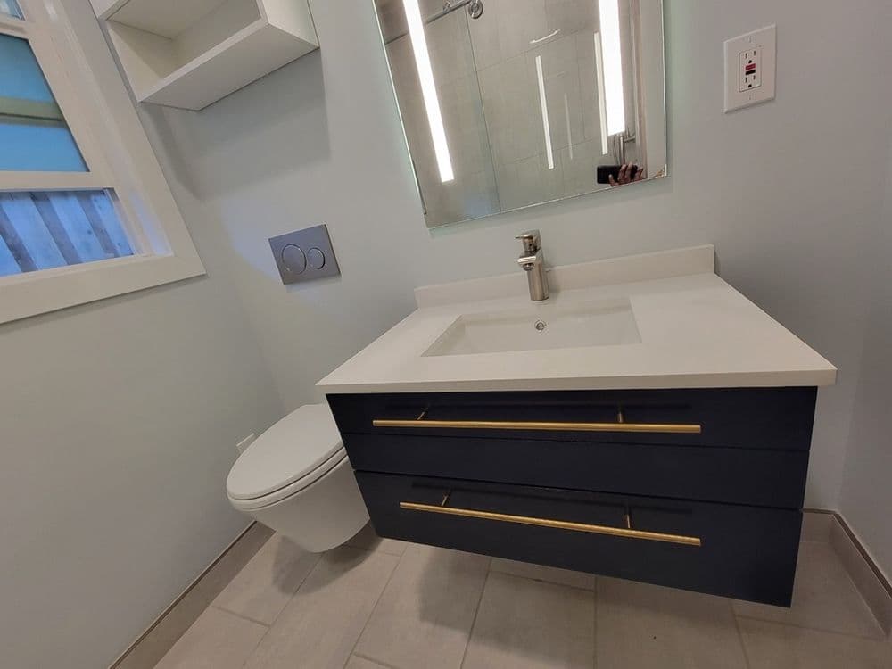 Modern bathroom with navy blue vanity, white sink, and sleek mirror, featuring elegant fixtures.