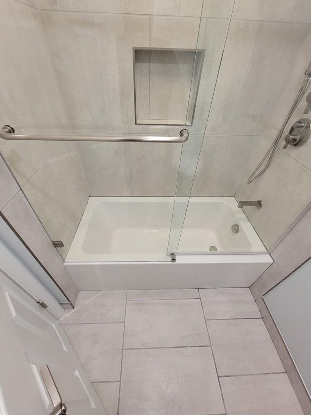 Modern bathroom with a glass shower door and a white bathtub against tiled walls.