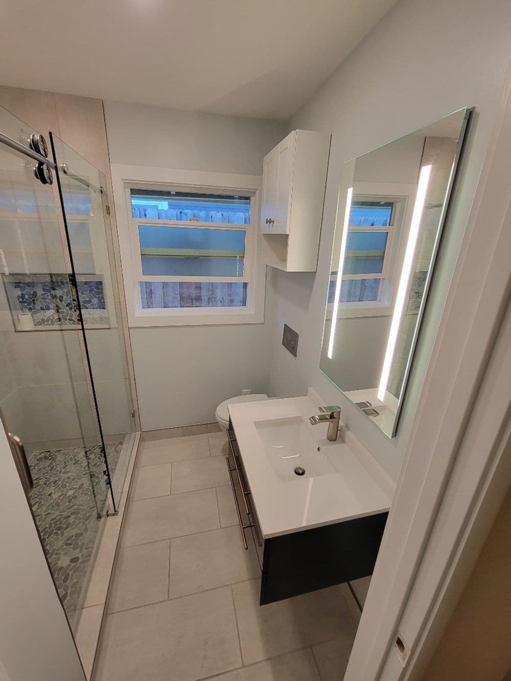 Modern bathroom with glass shower, sleek vanity, and backlit mirror, featuring neutral tiles.