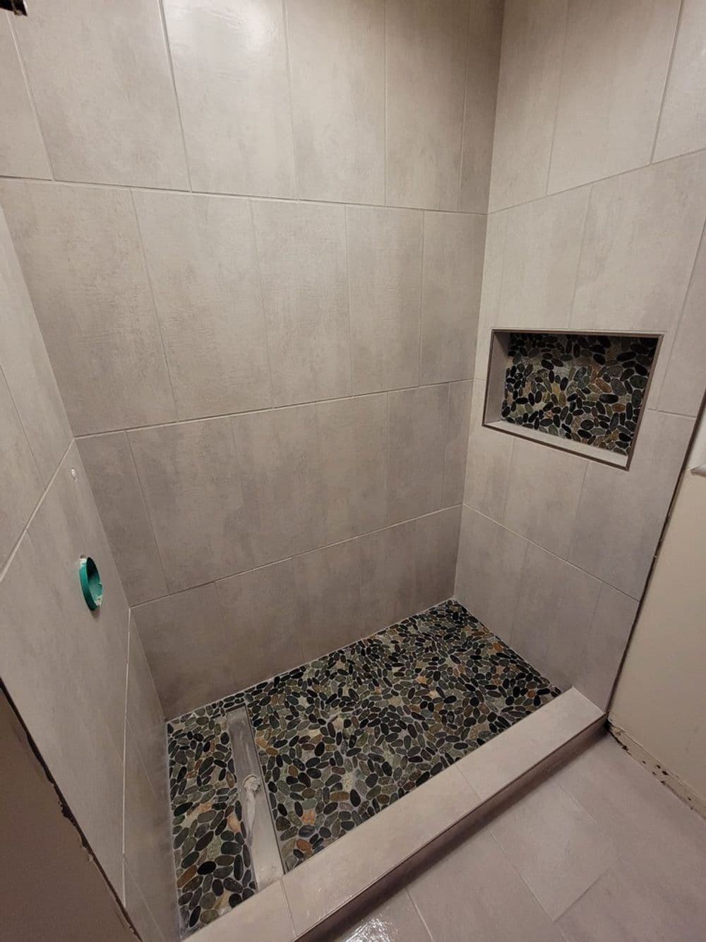 Modern shower design with gray tiles and a pebbled floor detail featuring a built-in niche.
