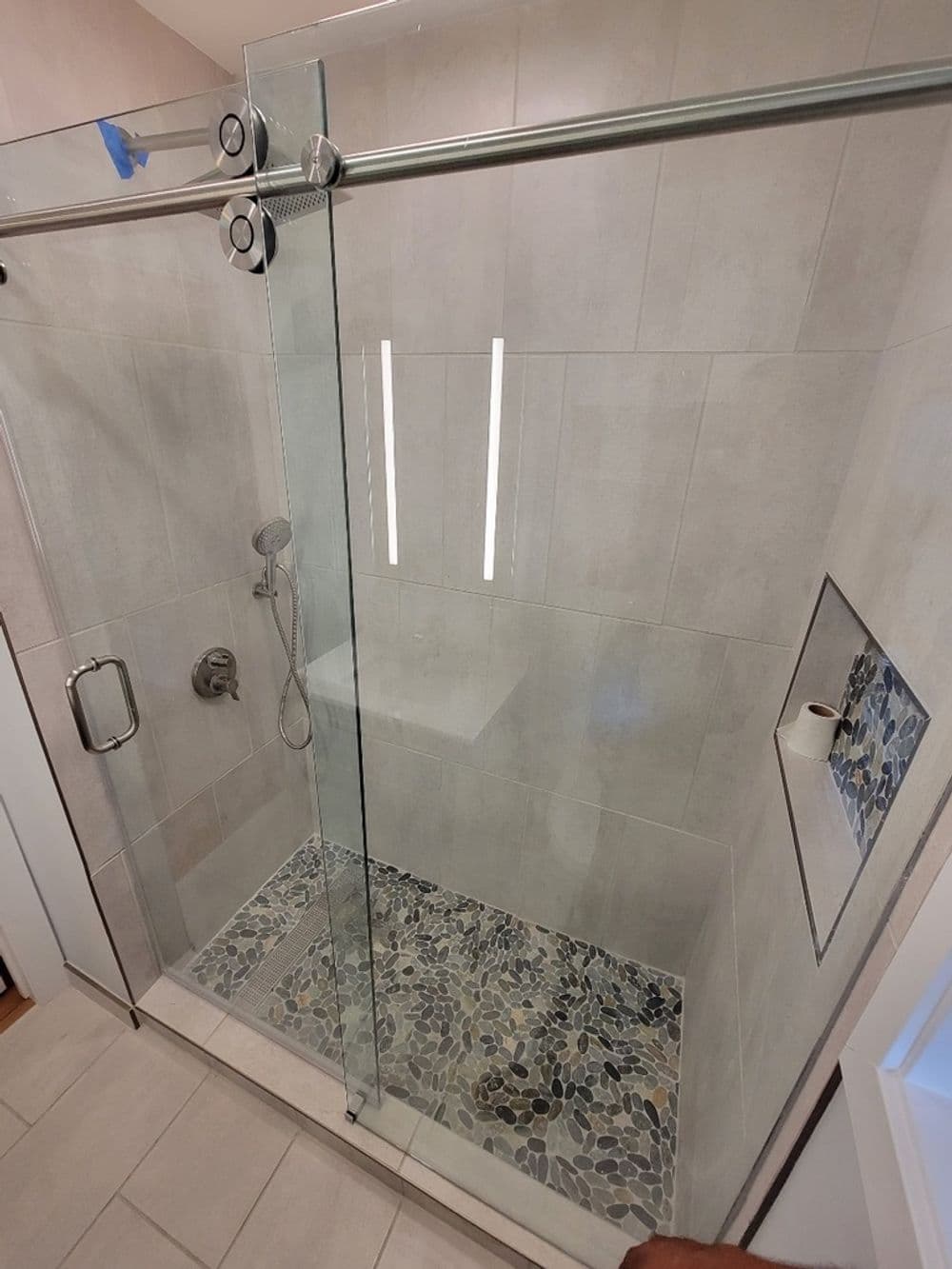 Modern walk-in shower with glass doors, pebble floor, and recessed lighting.
