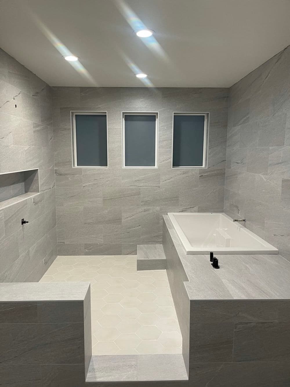 Modern bathroom featuring a freestanding tub, natural stone tiles, and three large windows.