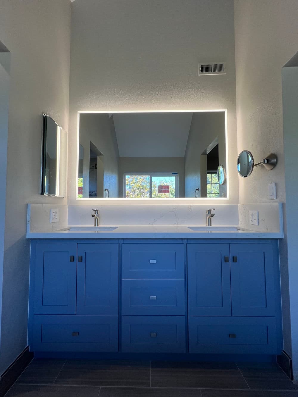 Modern blue bathroom vanity with double sinks, large mirror, and natural light.