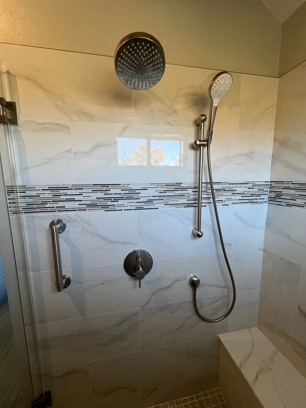 Modern shower with rainfall and handheld fixtures, marble tiles, and grab bars for accessibility.