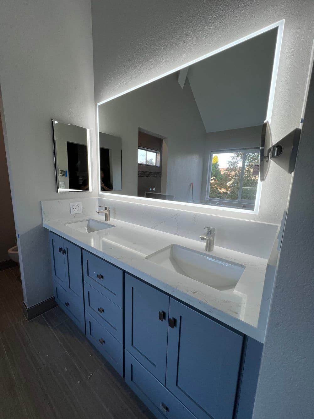 Modern bathroom with blue cabinetry, double sinks, and backlit mirror. Stylish and functional design.