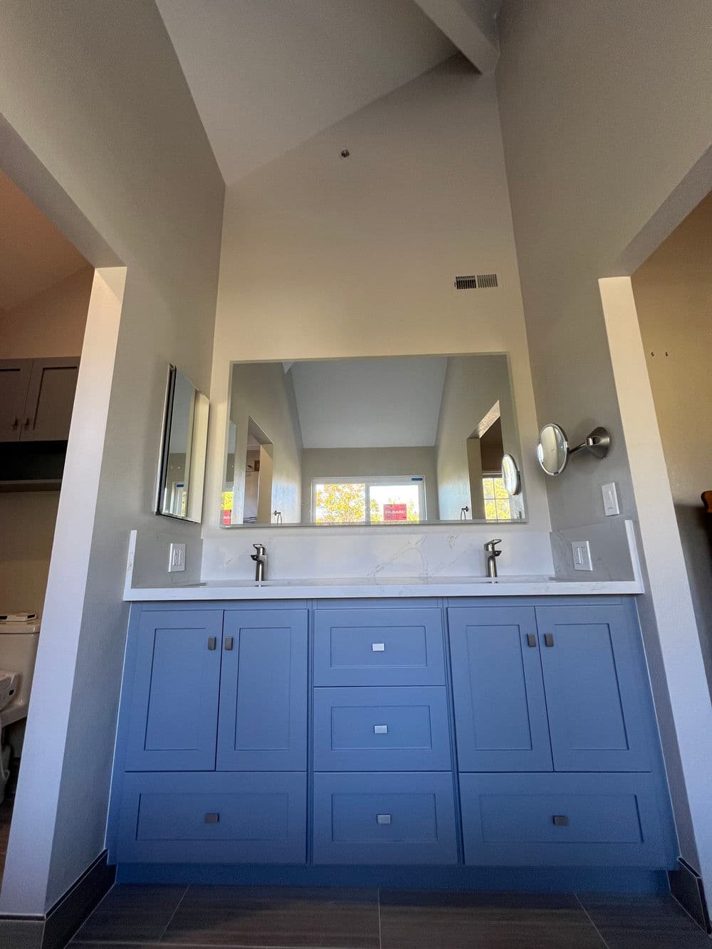 Modern bathroom design featuring a blue vanity, two mirrors, and natural light.