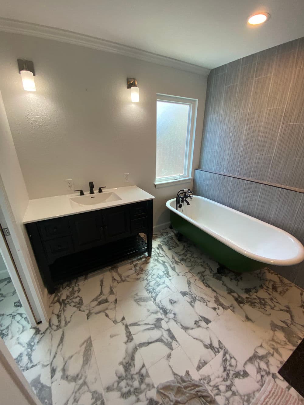 Modern bathroom featuring a freestanding green bathtub, marble floor, and stylish fixtures.