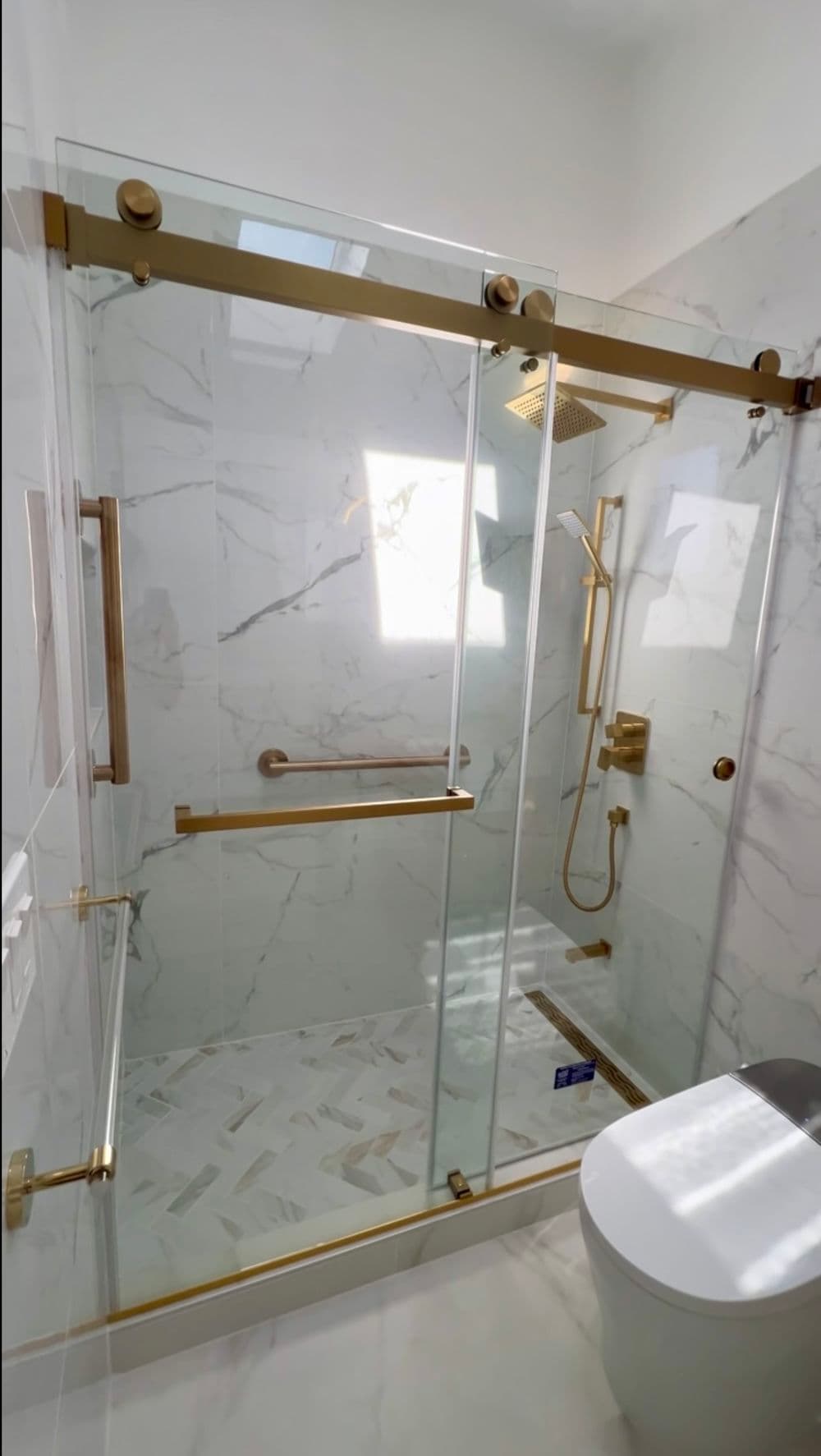 Modern bathroom with a glass shower enclosure and gold fixtures on marble tiles.