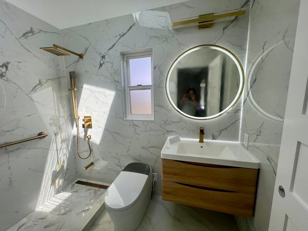 Modern bathroom featuring marble walls, circular mirror, gold fixtures, and sleek vanity.