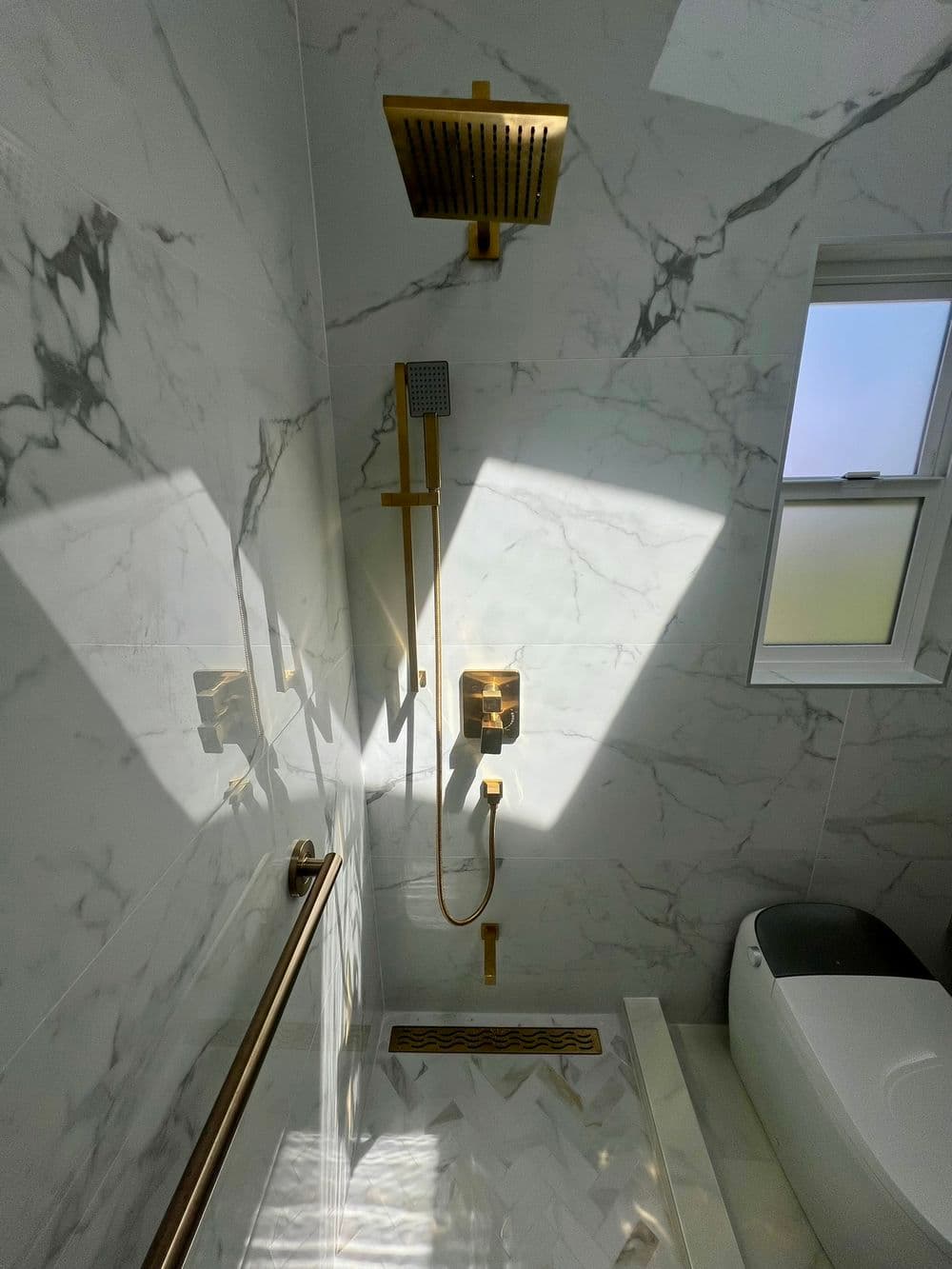 Luxurious marble bathroom with gold fixtures, modern showerhead, and natural light.