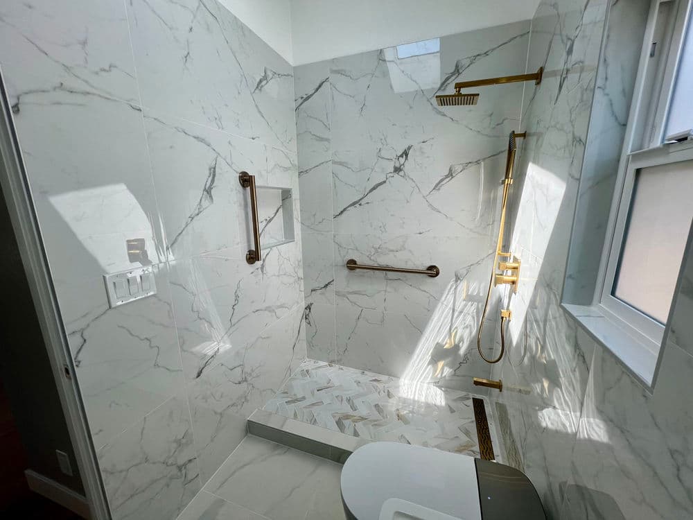 Luxurious marble shower with gold fixtures and natural light streaming in. Modern bathroom design.