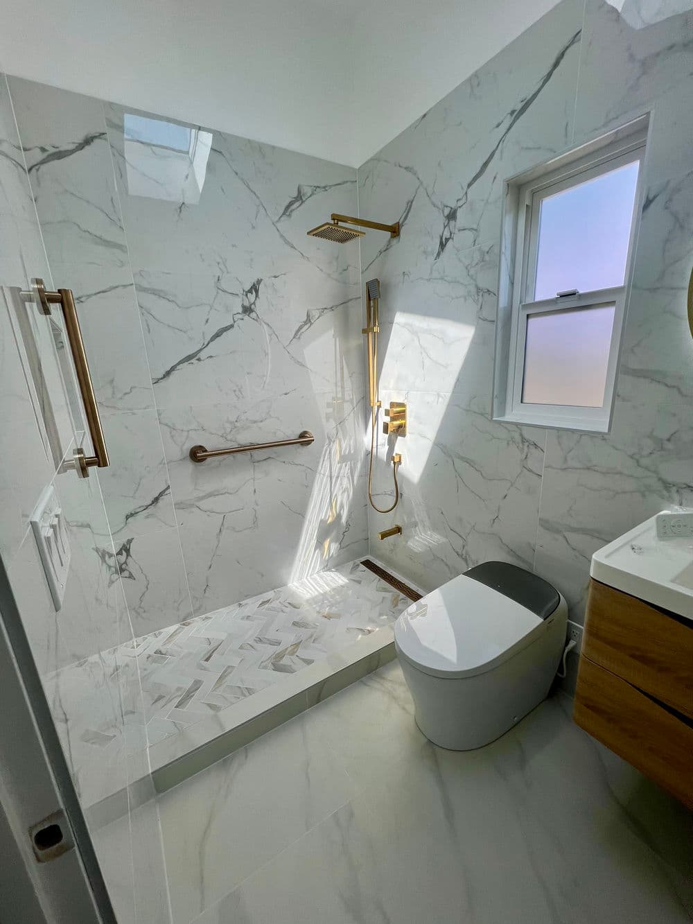 Modern marble bathroom featuring walk-in shower, gold fixtures, and sleek toilet design.