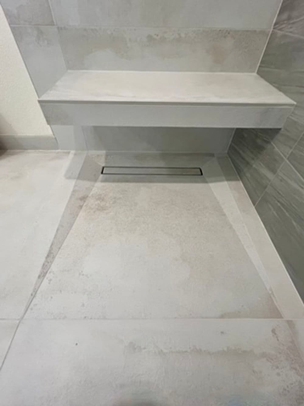 Modern bathroom with sleek gray tile flooring and a minimalist built-in bench.