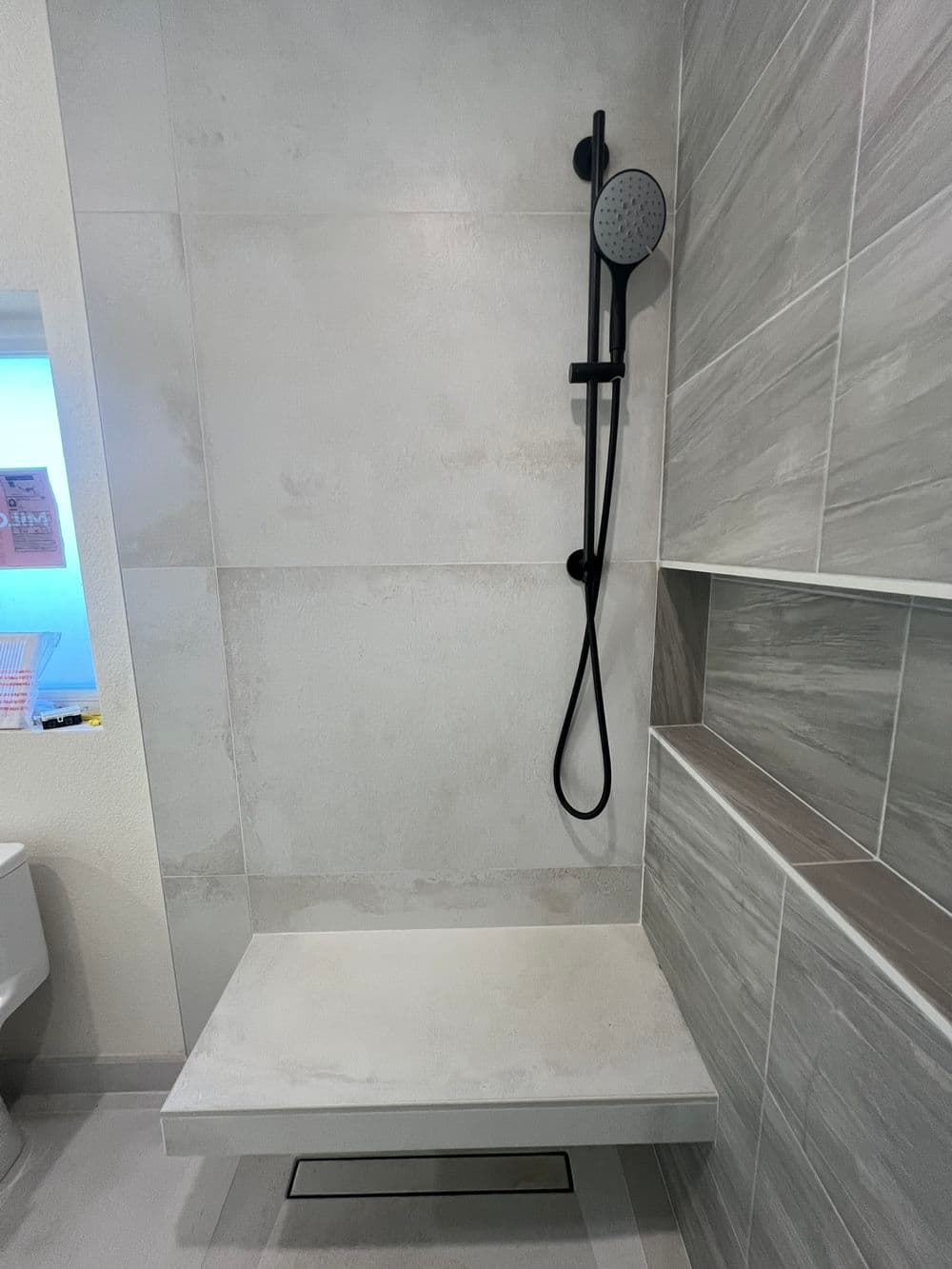 Modern shower space with a sleek black showerhead against gray tiled walls. Minimalist design.