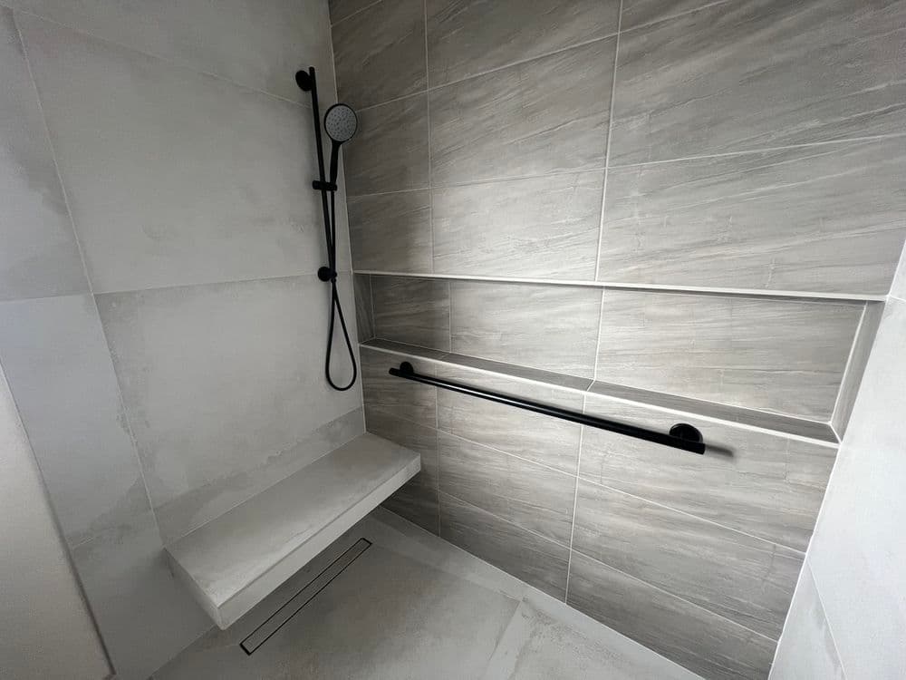 Modern shower with gray tiles, handheld showerhead, and built-in storage shelf.