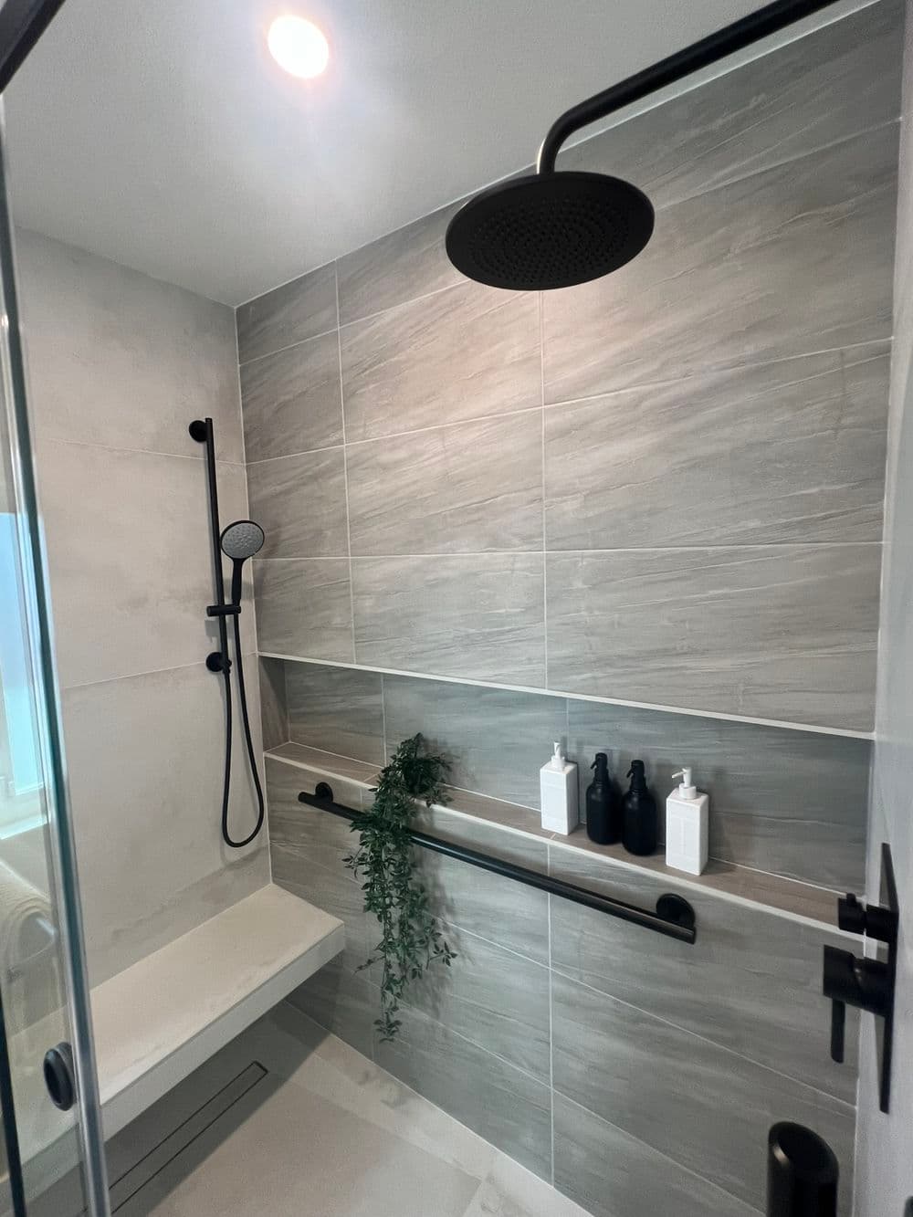 Modern bathroom shower with gray tiles, black fixtures, and stylish shelf for toiletries.