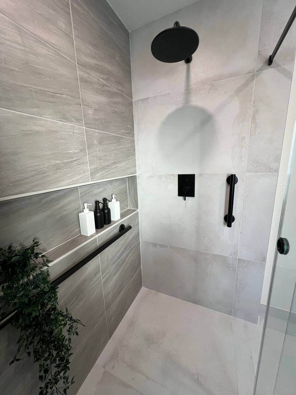 Modern shower design with gray tiles, black fixtures, and stylish toiletries on shelves.