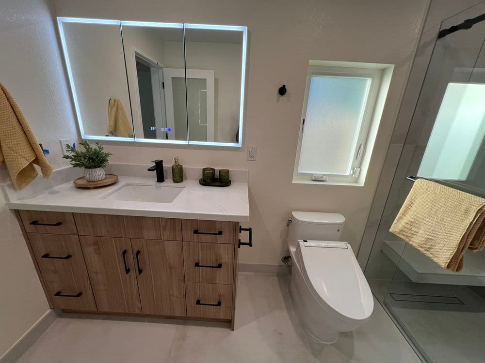 Modern bathroom with wooden vanity, mirror, shower, and large window for natural light.